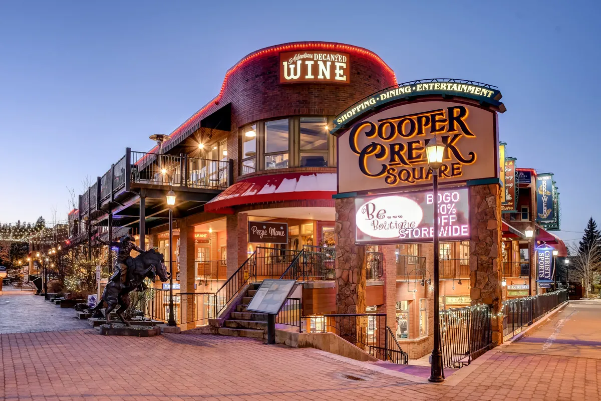 This exterior shot features the welcoming Cooper Creek Square with a prominent sign, inviting wine shop, outdoor seating, and festive lighting. The area exudes a lively, communal vibe ideal for shopping, dining, and family outings.