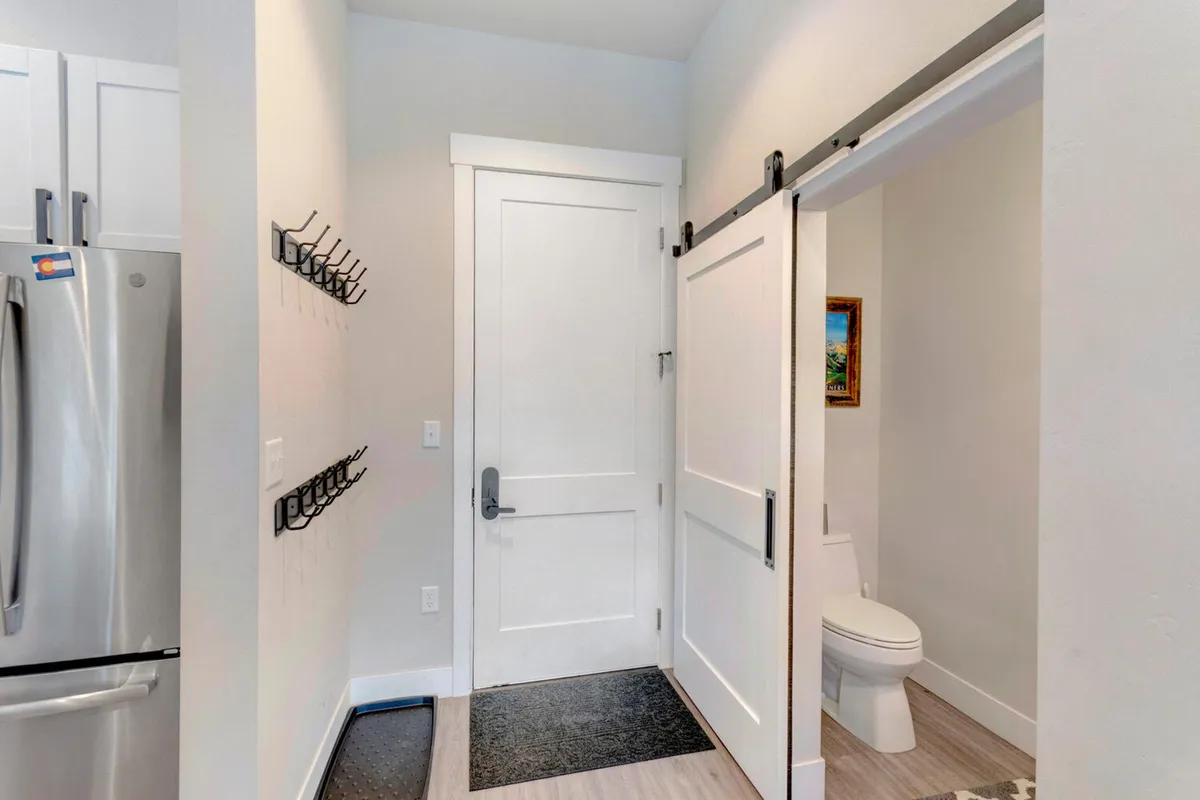 A stylish sliding barn door marks the entry point, with wall hooks for hanging coats and bags, a refrigerator just inside, and tasteful artwork. This vignette captures the functional and aesthetic qualities of the entry space, emphasizing practical storage and first impressions.