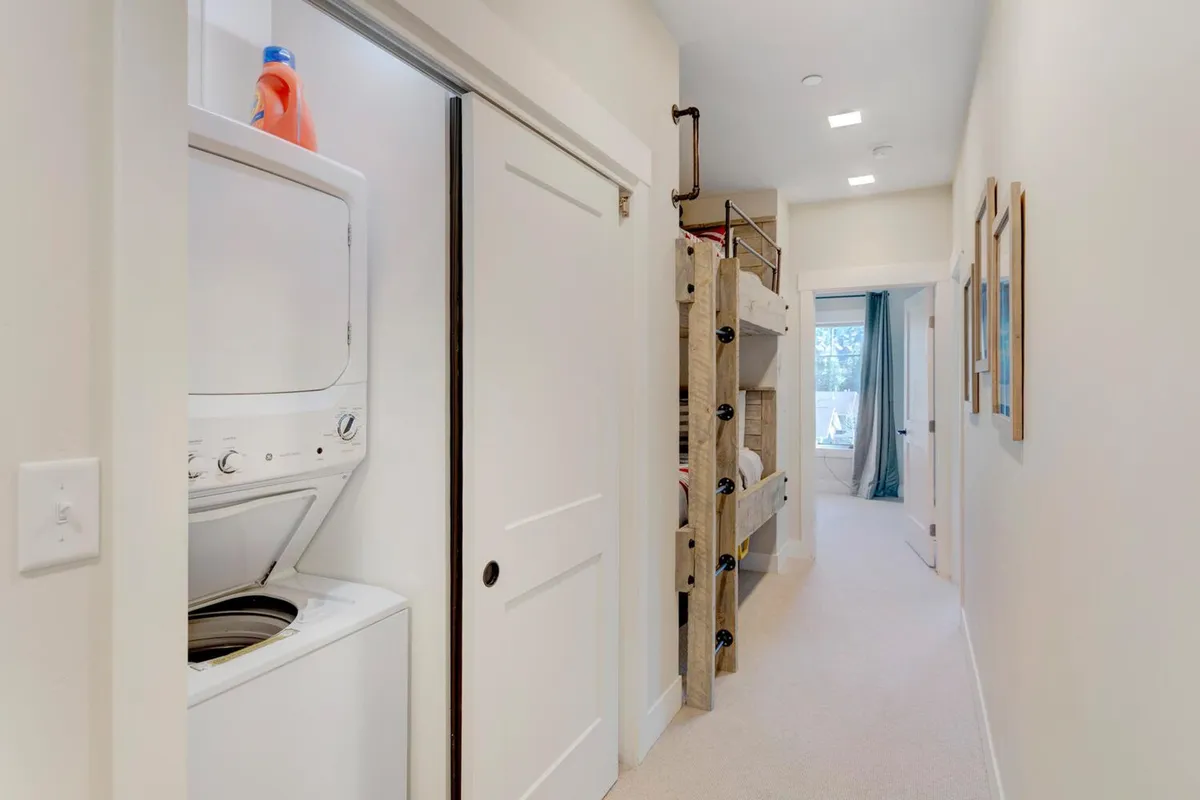 A hallway with an in-unit washer and dryer is visible, accompanied by a cozy bunk bed nook and decorative frames. The laundry area is neatly integrated, emphasizing convenience for refreshing outdoor gear and everyday clothing.