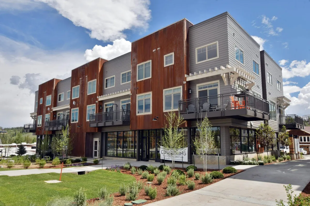 The exterior of a modern building featuring several balconies, landscaped gardens, and vibrant social spaces. The image suggests the blend of private and communal resort-style amenities.