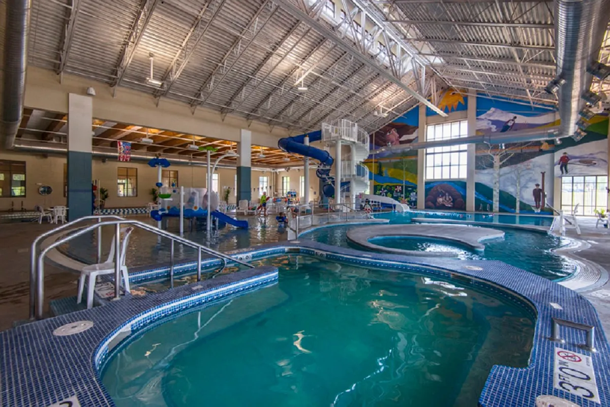 A vibrant indoor pool area featuring a large water slide, children actively playing in the water, and spaces for both excitement and relaxation. The atmosphere is lively, capturing the spirit of fun and adventure.