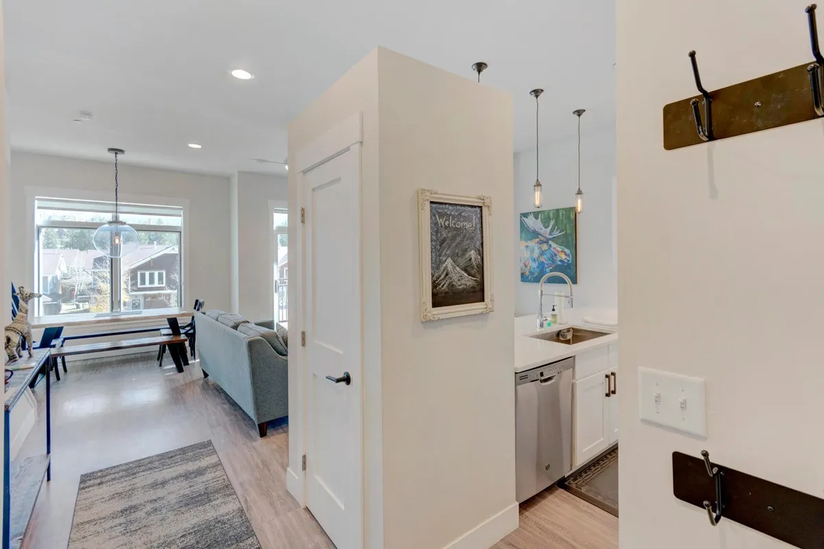 This image features a view of the kitchen area, comfortable living room seating, and a glimpse of the entryway decor. The entryway, though not the main focus, is visible and demonstrates how the space transitions from the outdoors into a welcoming, functional area for guests to arrive, remove coats and boots, and settle in.